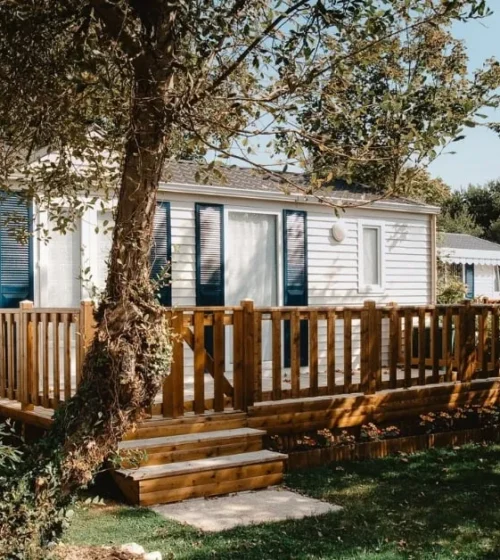 A cozy mobile home surrounded by greenery, featuring a wooden deck that enhances its inviting appeal.