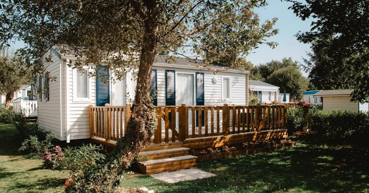 A cozy mobile home surrounded by greenery, featuring a wooden deck that enhances its inviting appeal.