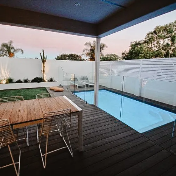 Elegant and secure glass pool fence surrounding a modern pool, with a nearby seating area.