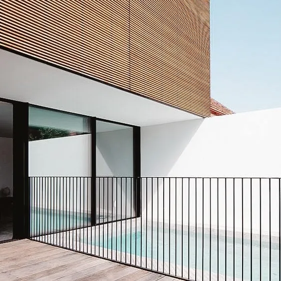 Modern pool fence with vertical metal bars alongside contemporary house with wood-slatted exterior and large windows