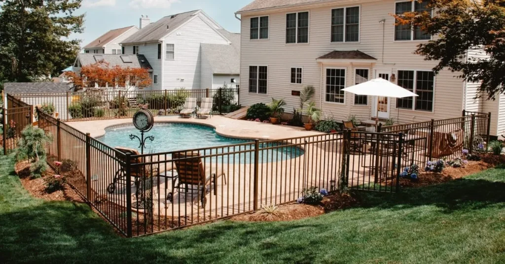 A backyard pool area featuring a well-maintained fence, lounge chairs, and vibrant landscaping, creating a stylish and secure environment.