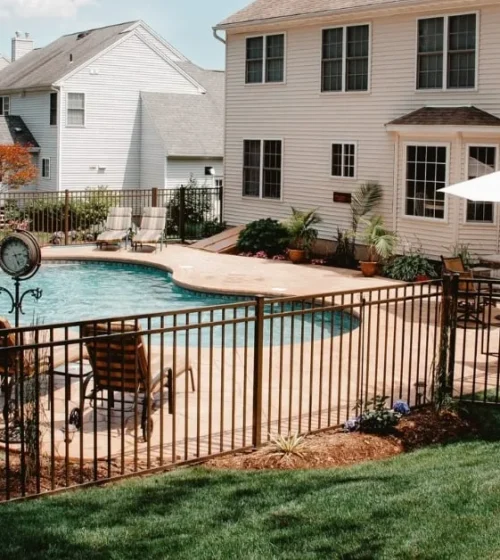 A backyard pool area featuring a well-maintained fence, lounge chairs, and vibrant landscaping, creating a stylish and secure environment.