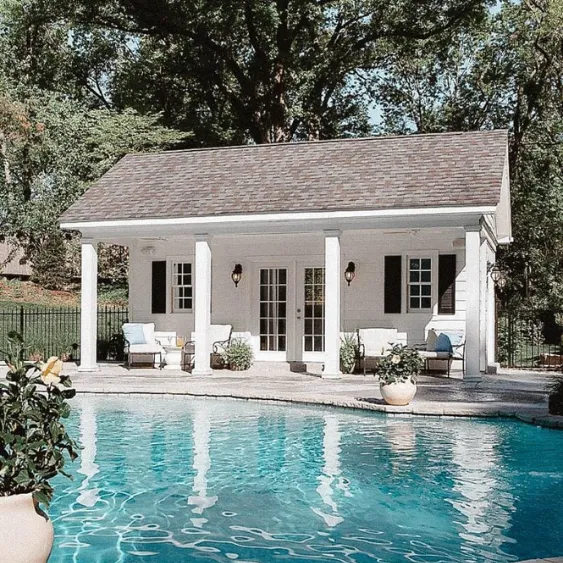 White pool house with classic columns and a sparkling pool in the foreground