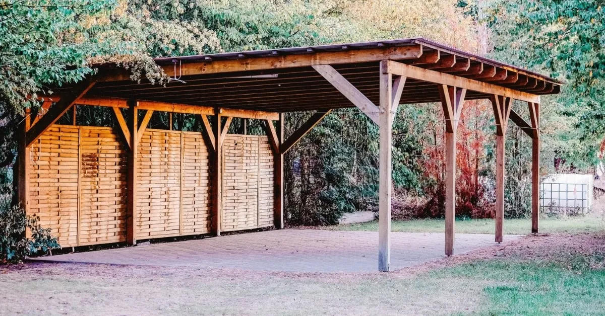 Wooden carport with a sturdy roof and privacy panels, set in a green, wooded backyard.