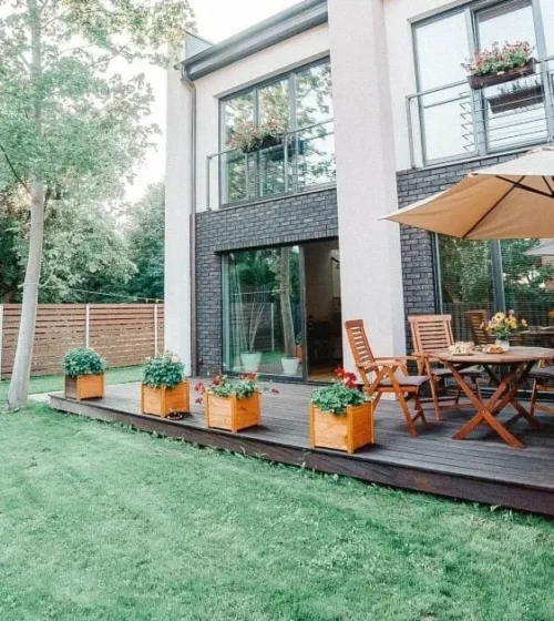 Modern backyard with a wooden deck, outdoor seating, and a stylish fence surrounding the green lawn.