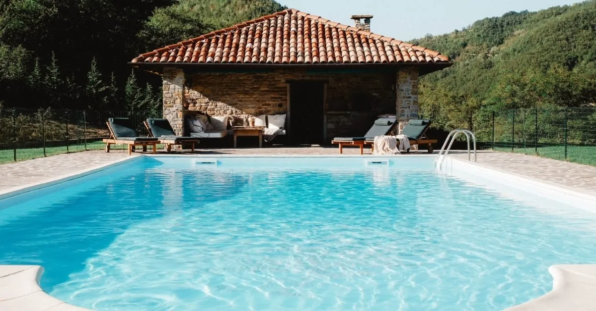 Pool house with a spacious pool surrounded by lush greenery.