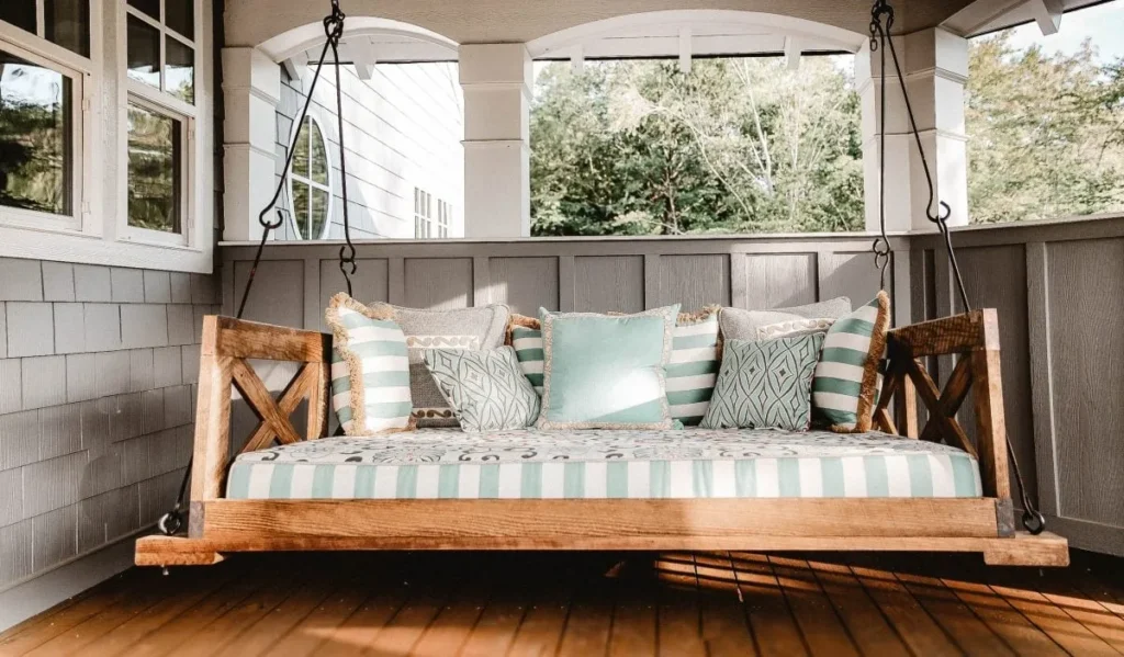 Cozy wooden porch swing with striped cushions and decorative pillows, creating a charming outdoor seating area on a deck.