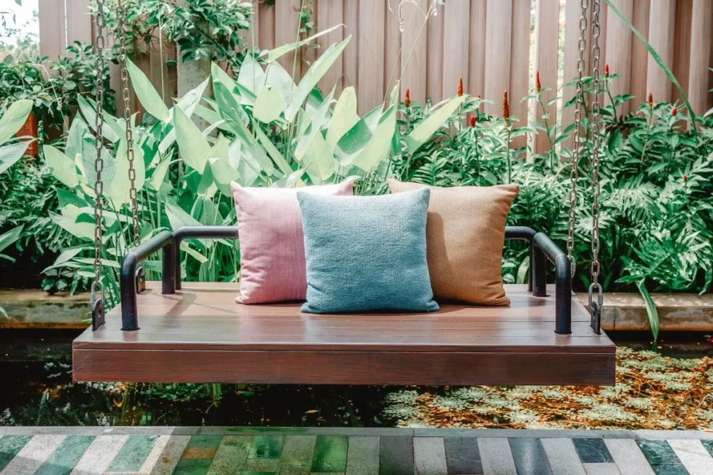 Modern outdoor swing with industrial-style metal frame and colorful cushions, set against a lush garden backdrop.