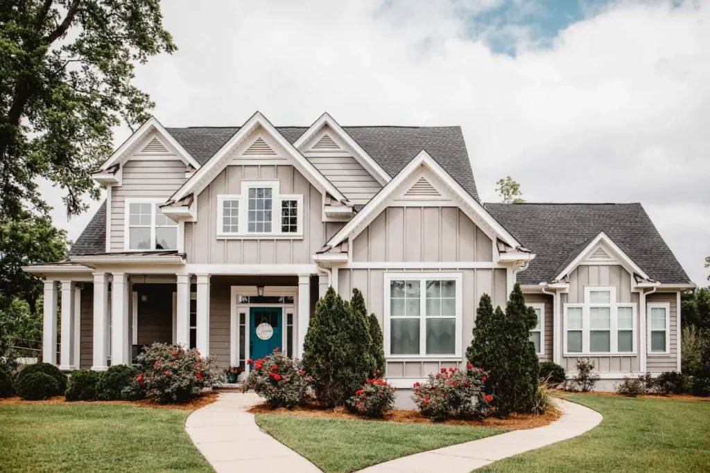 A charming two-story home with a welcoming front porch, lush landscaping, and a clear blue sky, showcasing potential for expansion.