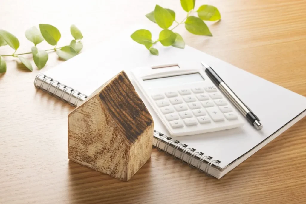 Notebook, calculator, and wooden house model on a desk.