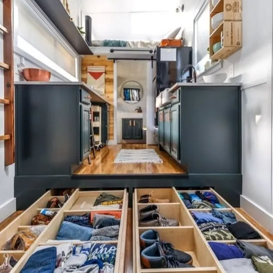 Interior of a tiny house with optimized space, featuring underfloor storage drawers and modern furniture to maximize space.