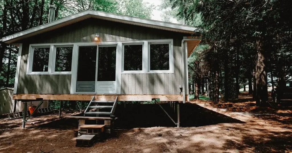 Petit chalet surélevé dans une zone boisée, soutenu par des pieux vissés, avec un escalier menant à l'entrée.