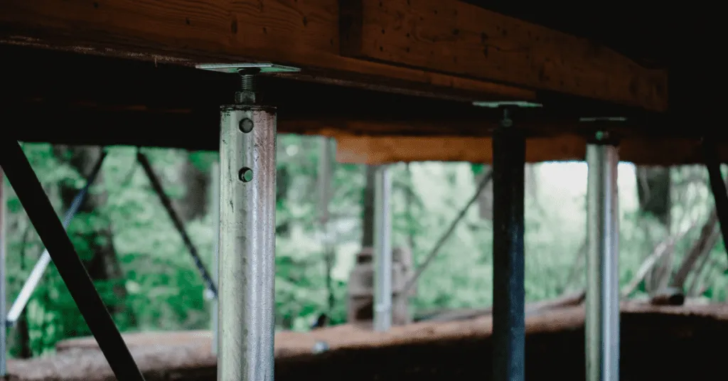 Screw piles supporting a wooden cabin foundation in a forest setting.