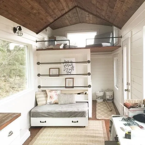 Cozy tiny house interior featuring a multifunctional bed with built-in storage, a lofted sleeping area, and smart shelving solutions.