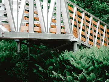 White metal boardwalk with wooden railings and eco-friendly screw pile foundations, seamlessly integrated into a lush green environment.