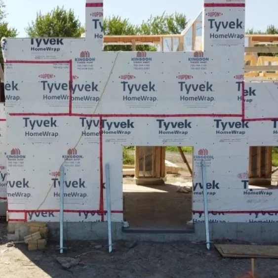 Partially constructed house wrapped in Tyvek, supported by screw piles.