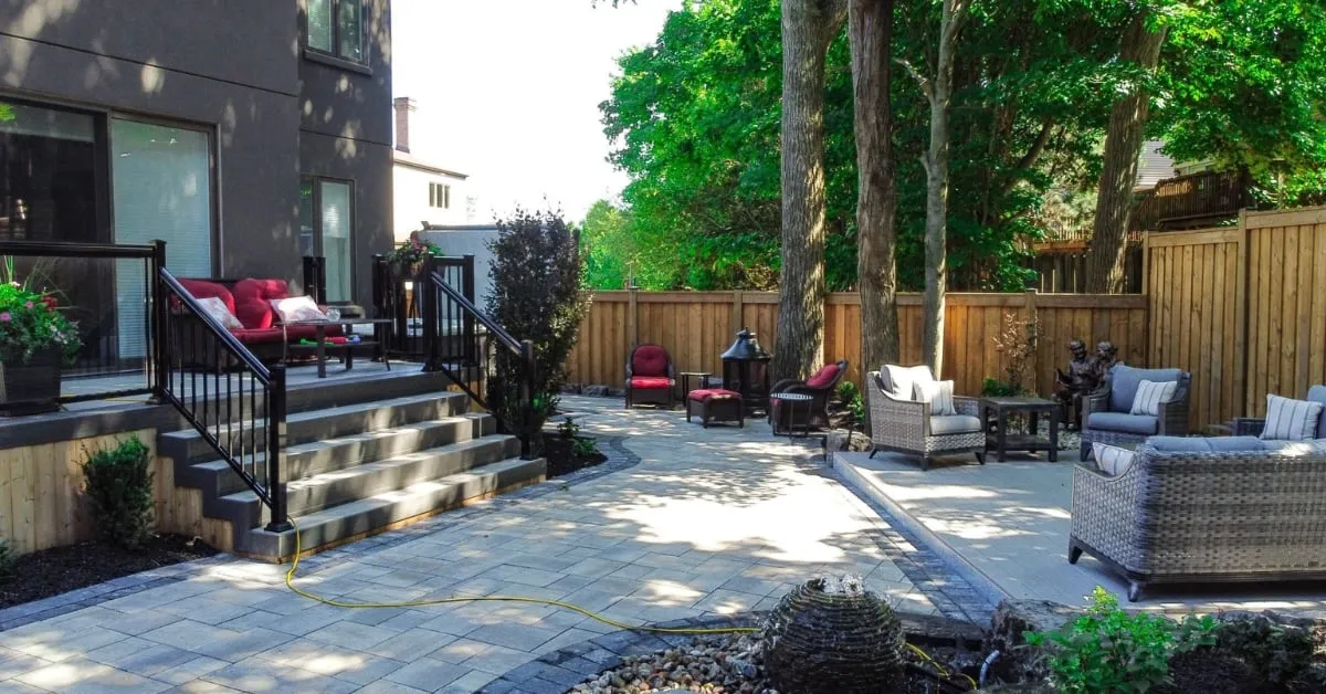 Modern backyard patio with comfortable seating, surrounded by trees and wooden fencing, featuring a well-constructed stairway leading to a deck.