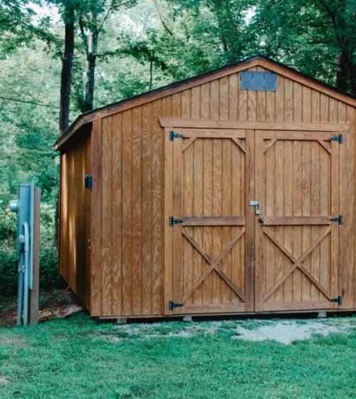 Wooden garden shed with large double doors, located in a lush green forest setting.