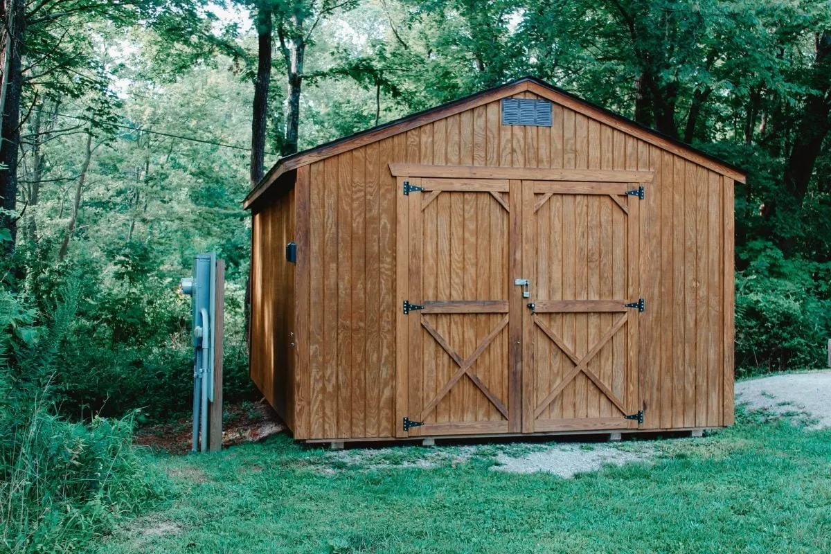 Wooden garden shed with large double doors, located in a lush green forest setting.