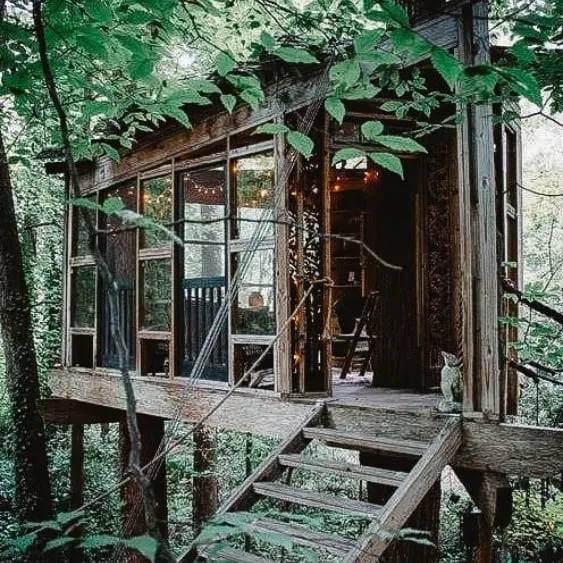 Rustic treehouse cabin nestled in a dense forest, elevated on stilts with string lights and large windows.