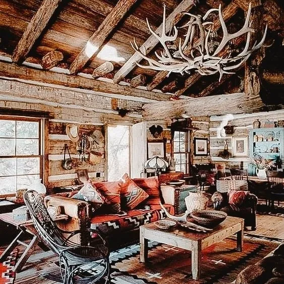 Rustic cabin interior featuring wooden beams, a cozy living space with patterned cushions, and a decorative antler chandelier.