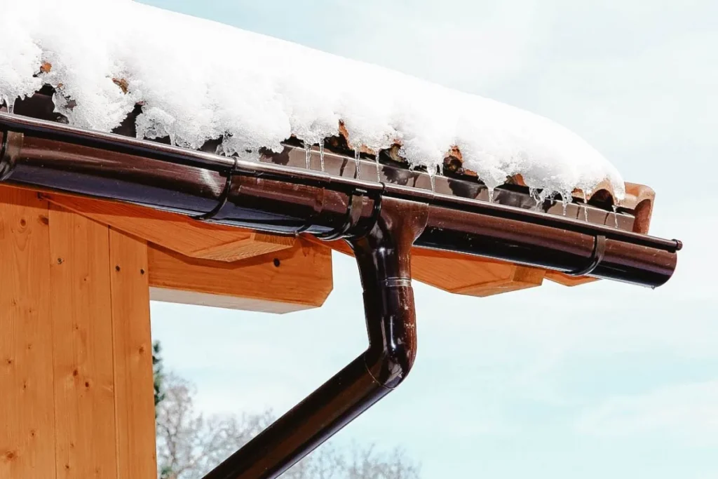 Snow-covered roof with icicles forming on a black gutter system.