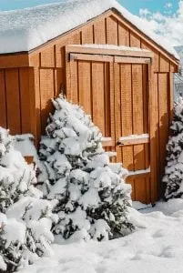 Wooden shed surrounded by snow-covered trees, set in a snowy winter landscape.