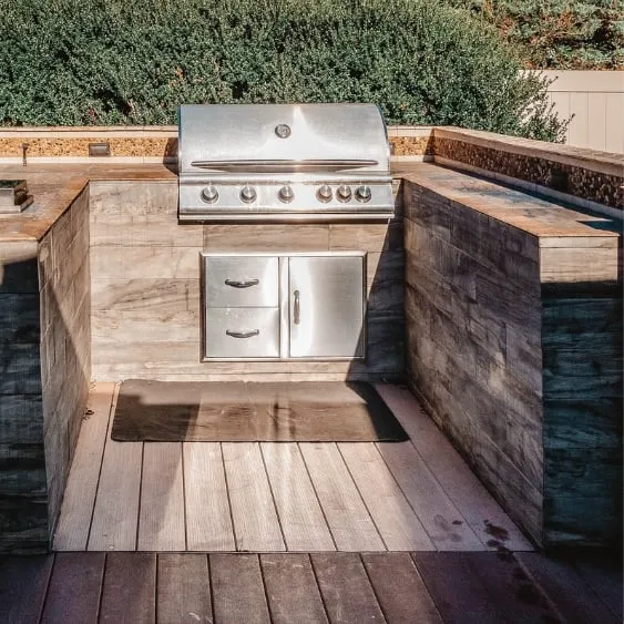 Outdoor kitchen with a built-in stainless steel grill, set in a wooden deck with surrounding countertops.