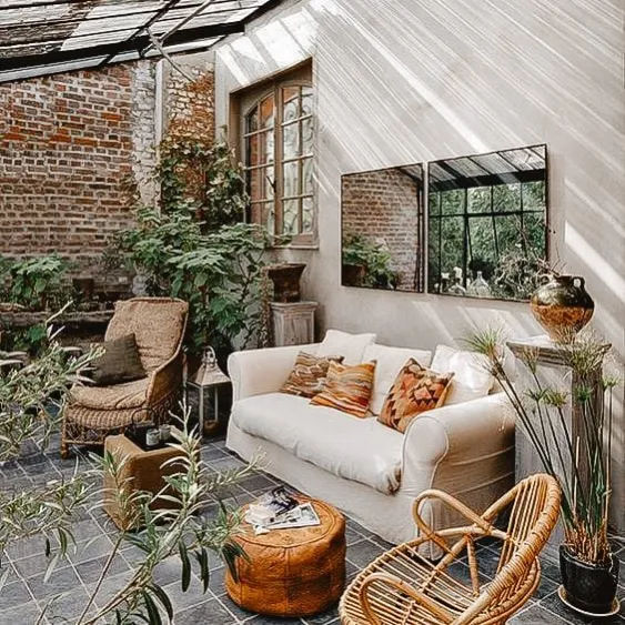 Cozy sunroom with natural light streaming in, featuring comfortable seating, plants, and a rustic brick wall.