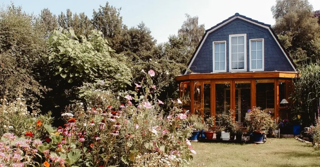 A charming sunroom attached to a cozy house with a lush garden in full bloom. The sunroom features large glass windows, allowing plenty of natural light to filter into the space, creating a peaceful garden retreat.