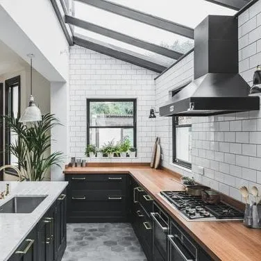 Modern kitchen with dark cabinets, wooden countertops, and a large skylight, creating a bright and open space.