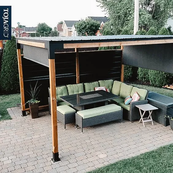 Modern pergola with a comfortable outdoor seating area featuring green cushions and a table, built on a brick patio.