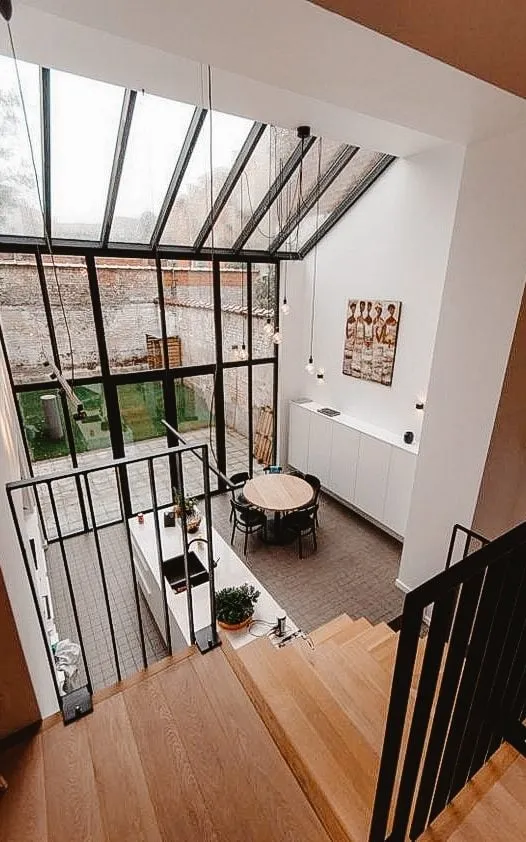 Extension moderne de maison avec de grandes fenêtres vitrées, une cuisine ouverte et une salle à manger, vue depuis un escalier.