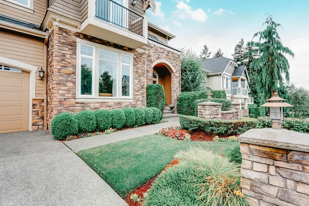 Front view of a modern house with a stone facade, manicured lawn, and landscaped garden path.