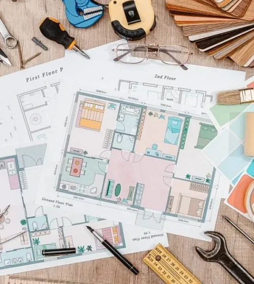 Home renovation tools, floor plans, paint swatches, and color samples spread on a wooden surface.