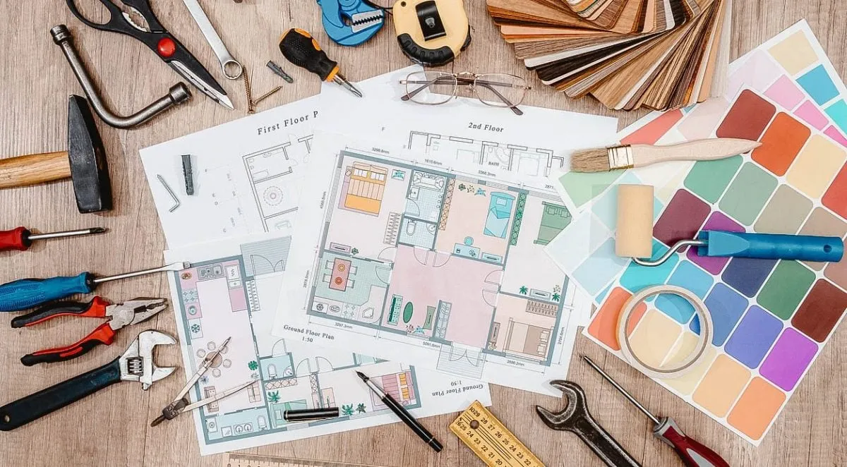 Home renovation tools, floor plans, paint swatches, and color samples spread on a wooden surface.