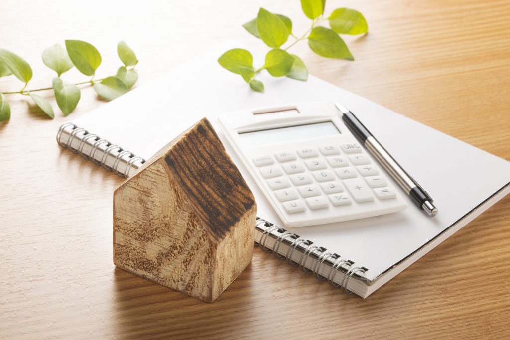 Wooden house and calculator to illustrate the planification of a home addition.