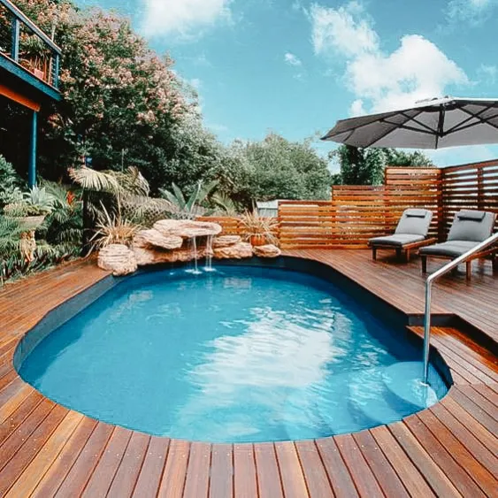 Luxurious backyard pool with wooden deck, possibly supported by screw piles, featuring lounge chairs, umbrella, and lush landscaping