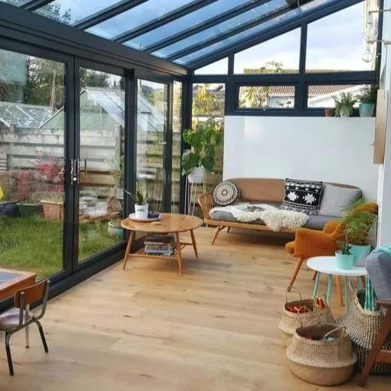 Solarium lumineux avec mobilier scandinave, toit en verre et vue sur un jardin verdoyant.