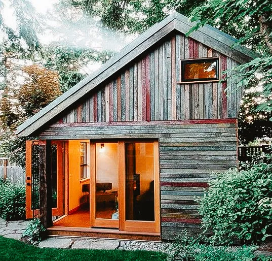 Charming wooden tiny house with large sliding doors and a warm interior glow.