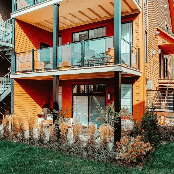 Two-story residential building with glass railings and vibrant orange siding, supported by black steel columns.