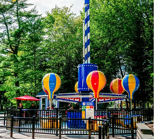 Colorful hot air balloon-themed amusement ride at Santa's Village, set against a backdrop of lush green trees.