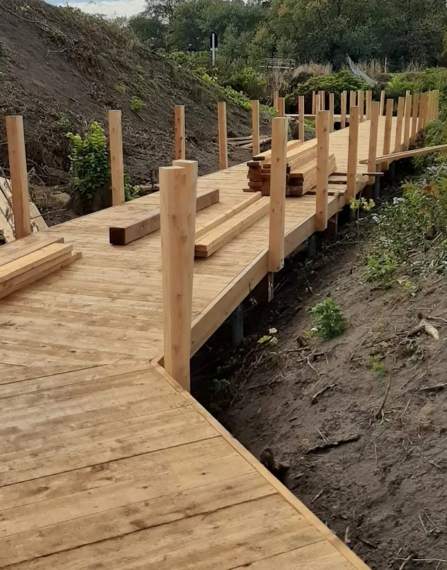 Wooden boardwalk under construction, elevated on screw piles, as part of a historical trail renovation project.