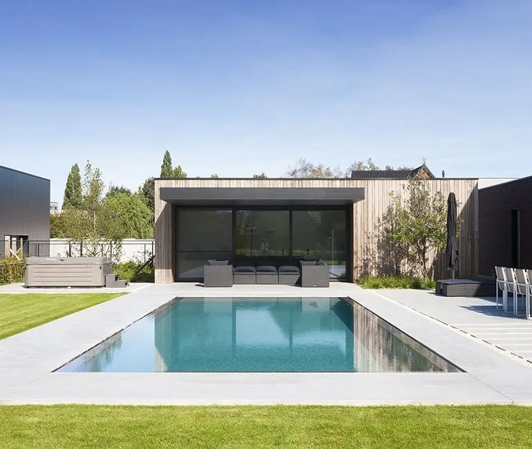 A modern pool house with a sleek swimming pool in front, featuring clean architectural lines and a wooden facade, situated in a landscaped backyard.