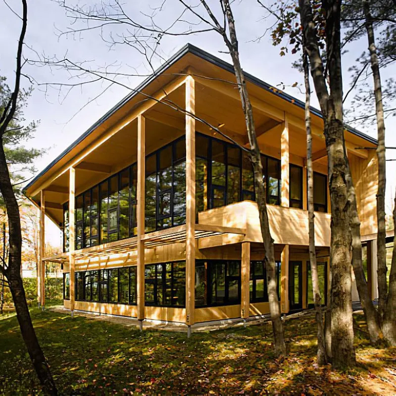 Modern wooden building with large glass windows in a forest setting.