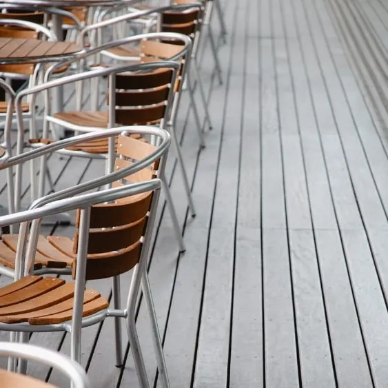 Rangées de chaises extérieures modernes avec assises en bois et structures métalliques, disposées sur un pont en bois élégant.