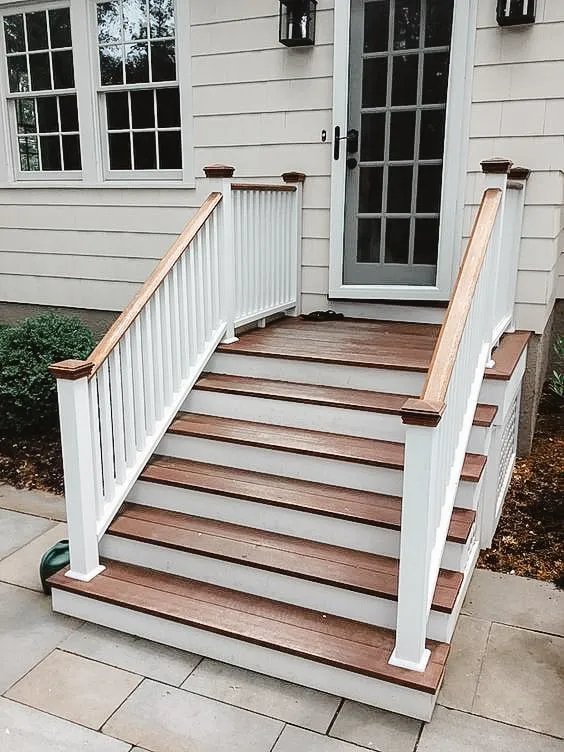 Traditional wooden outdoor stairs with white railing and wooden handrails leading to a home entrance.