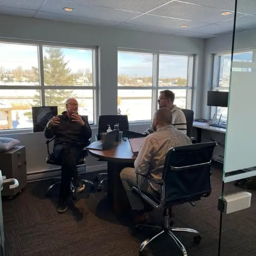 Three Postech Screw Piles employees having a meeting in a bright office space with large windows.