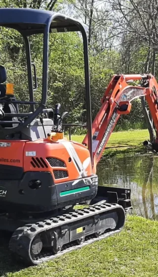 Excavateur Postech effectuant l'installation de pieux vissés près d'un plan d'eau, illustrant l'efficacité et la précision dans des environnements variés.